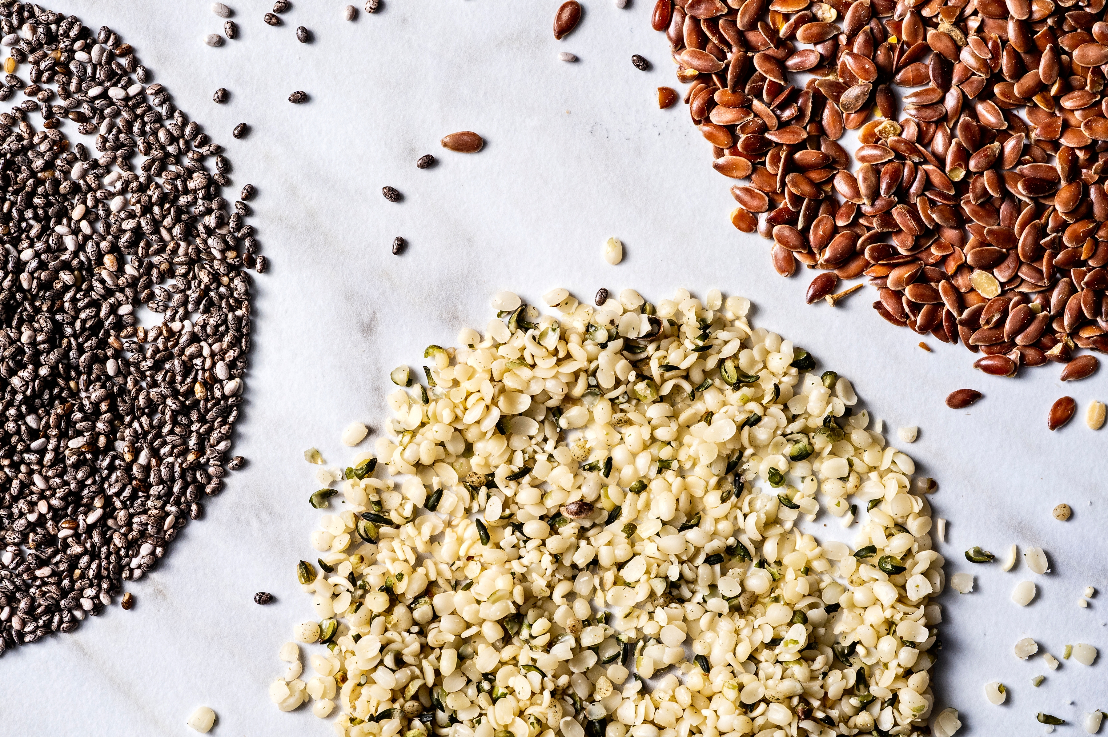 Top-down view of chia, sesame, flax, and hulled hemp seeds arranged in small piles on a textured surface